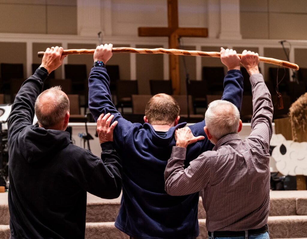 The Art of Drawing Readers In: Your attractive post title goes here Three men raise a wooden staff in a church setting with a cross visible in the background.